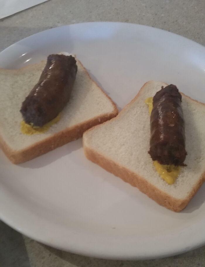Two sausage links with mustard on plain white sandwich bread, an example of outrageous meals not matching menu photos
