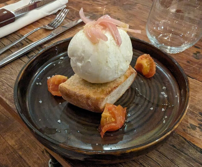 Plate with a scoop of cheese on toasted bread topped with pickled onions and small tomato pieces, showcasing outrageous meal presentation.