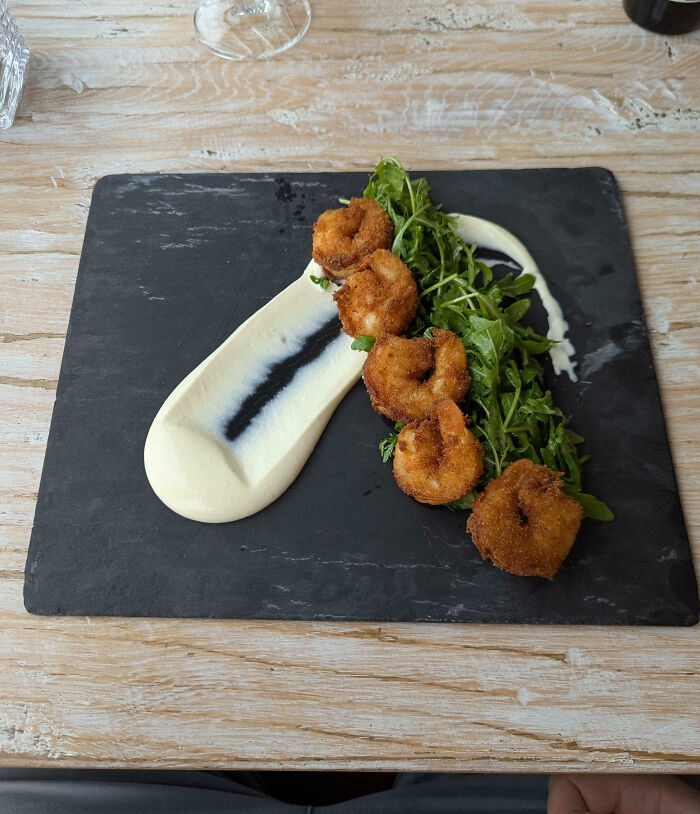 Breaded shrimp served with sauce and greens on a black slate plate from outrageous meals that look nothing like menu photos