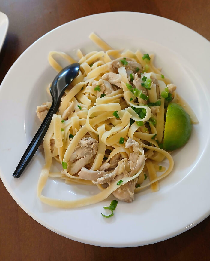 Plate of plain pasta with chicken and green garnish alongside a lime wedge, an example of outrageous meals versus menu photos.