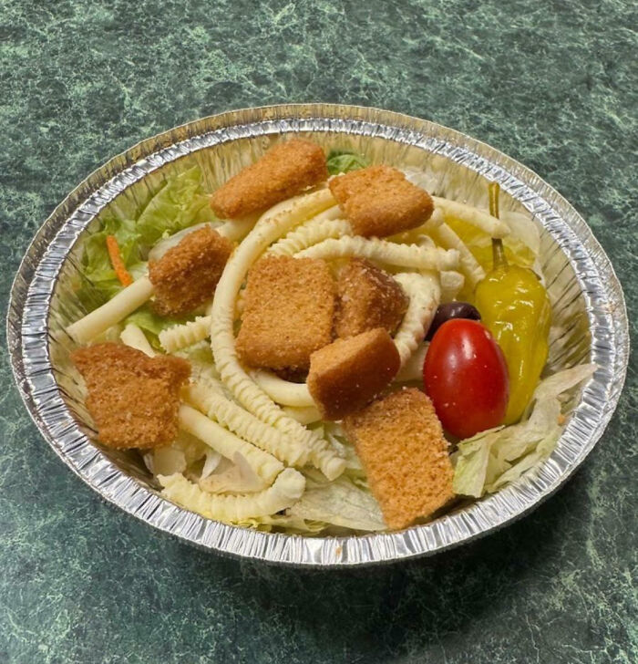 Salad with crinkle-cut fries, croutons, lettuce, cherry tomato, and pepper in a foil container, example of meal difference.