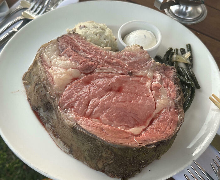 Outrageous meal featuring an oversized, undercooked prime rib with mashed potatoes and green beans on a white plate.