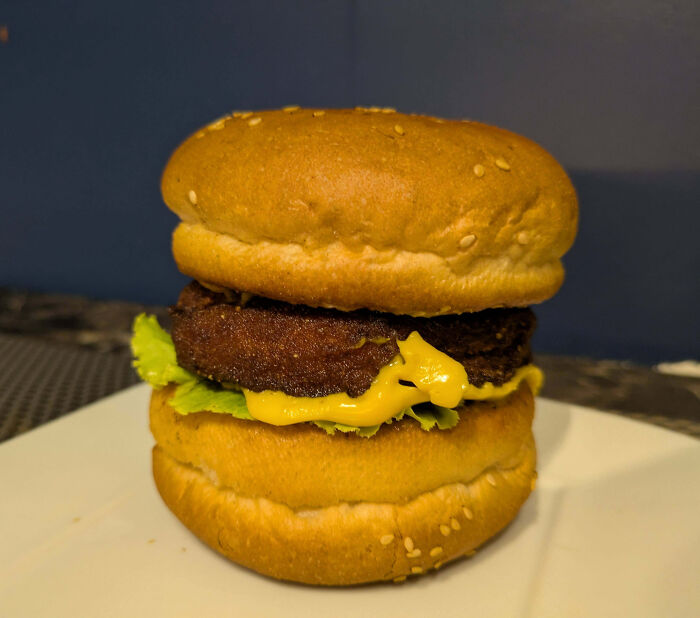 A homemade burger with uneven layers of cheese, lettuce, and patties, showcasing outrageous meals not matching menu photos.