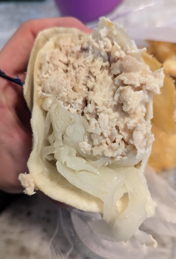 Hand holding a poorly made meal with unappetizing filling, an example of outrageous meals not matching menu photos.