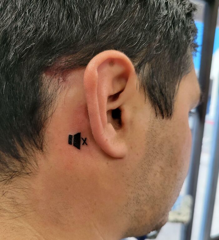 Small wholesome tattoo of a muted speaker icon behind the ear, showing how little ink can carry a lot of meaning. Small wholesome tattoo of a muted speaker icon behind the ear, showing how little ink can carry a lot of meaning.