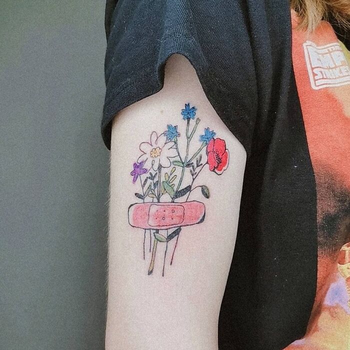 Colorful wholesome tattoo of flowers and a pink bandage on the inner arm, showing how a little ink carries meaningful art.