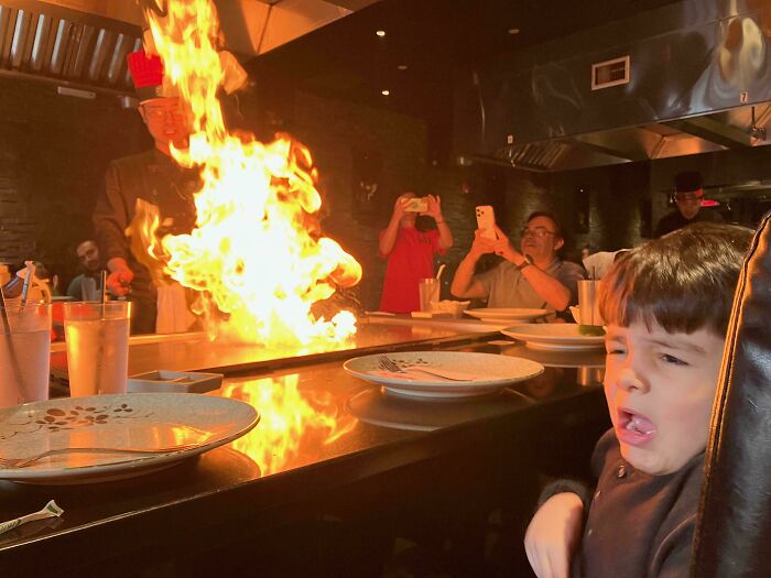 Child making a funny face at a teppanyaki grill with a large flame, a perfect time funny and weird pic.