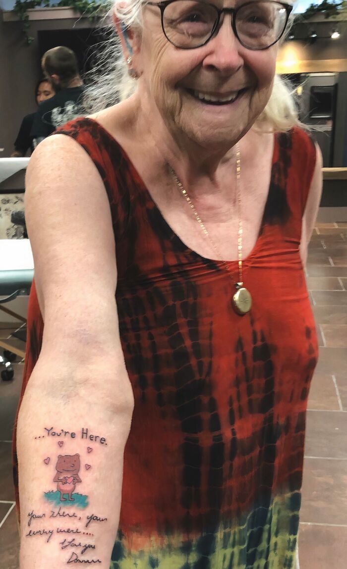 Elderly woman smiling and showing a wholesome tattoo on her forearm with meaningful ink and cute design.