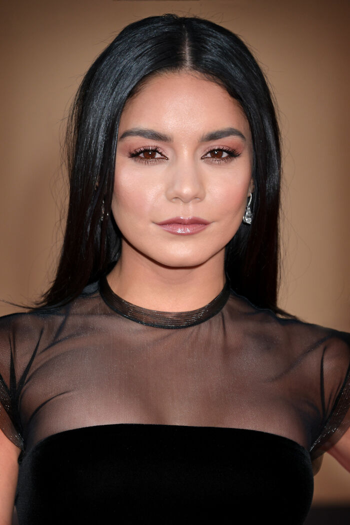 Vanessa Hudgens with sleek black hair and subtle makeup, wearing a sheer black top at a formal event