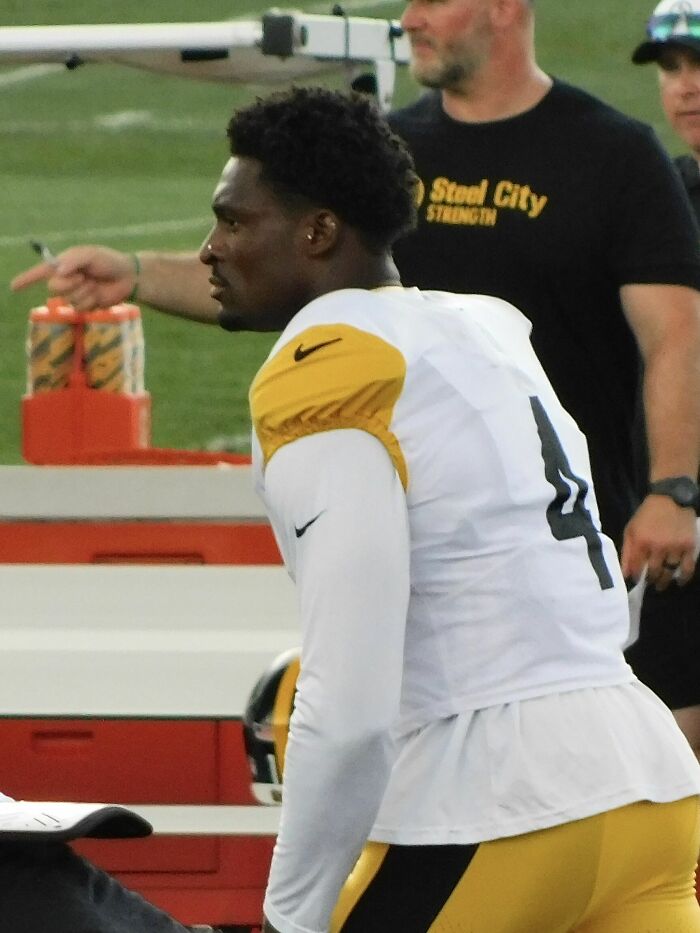 DK Metcalf in football uniform on sidelines during practice, focusing on training and game preparation.