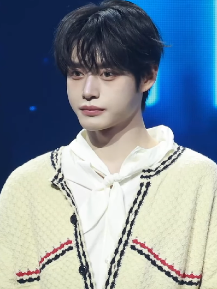 Kim Ji-woong on stage, wearing a cream cardigan and white shirt, showcasing his career highlights in entertainment.