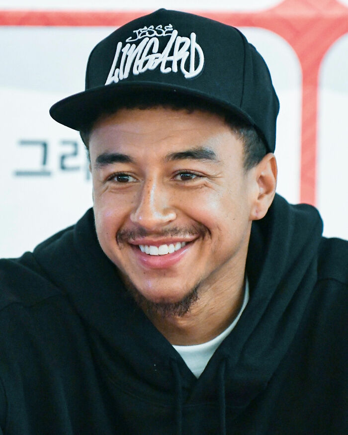 Jesse Lingard smiling, wearing a black cap with his name, dressed in a black hoodie during a public appearance.