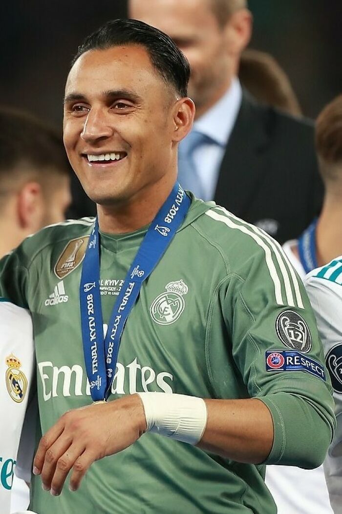 Keylor Navas smiling in Real Madrid goalkeeper kit with 2018 Champions League final medal around his neck.