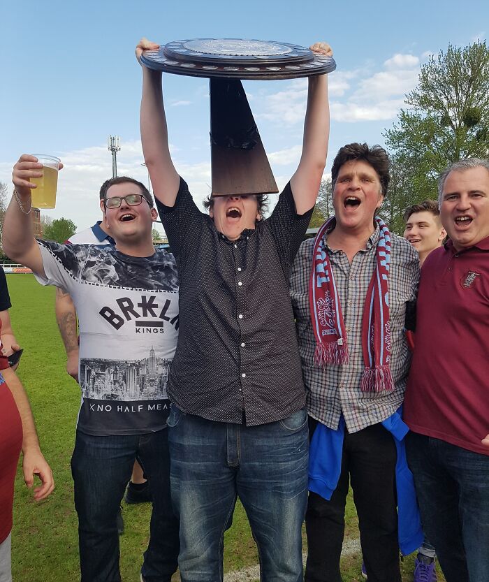 Group of men celebrating on a field with a trophy perfectly covering one man's face in funny, interesting, and weird pics.