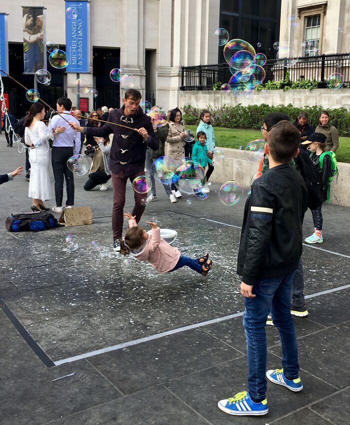 Man creating giant bubbles as child appears to float mid-air surrounded by kids in a funny, interesting and weird pic.
