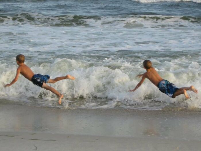 Two boys captured mid-air diving into ocean waves, a funny and interesting perfect timing beach picture.