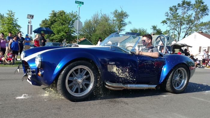Blue classic car splashing water as it drives by a crowd, captured in a perfectly timed funny and interesting pic.