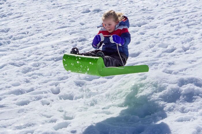 Child in winter clothes caught mid-air on a green sled, a funny and interesting perfect timing action shot in the snow.