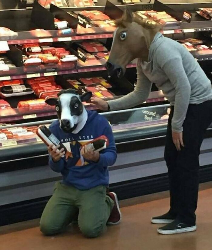 Two people wearing animal masks shopping in a Walmart meat section, creating a strange and confusing scene.