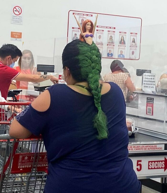 Woman with green braided hair styled with a doll on top shopping inside a Walmart store checkout area.
