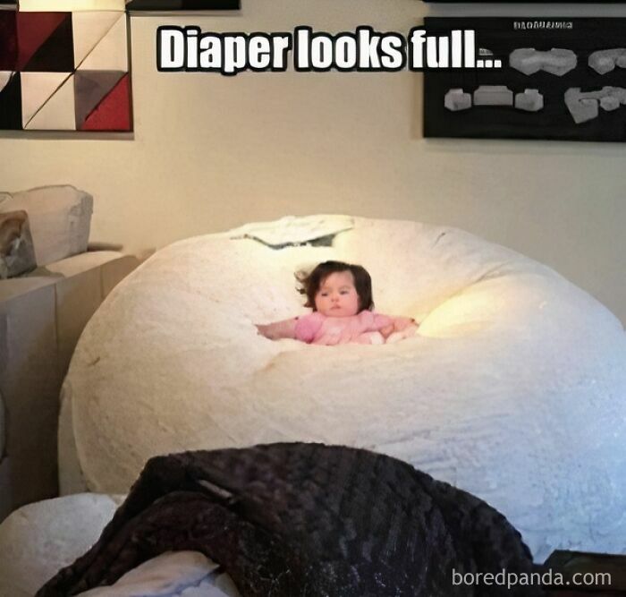 Baby sitting in a large beanbag chair with text about a full diaper, relatable memes for parents going through it.
