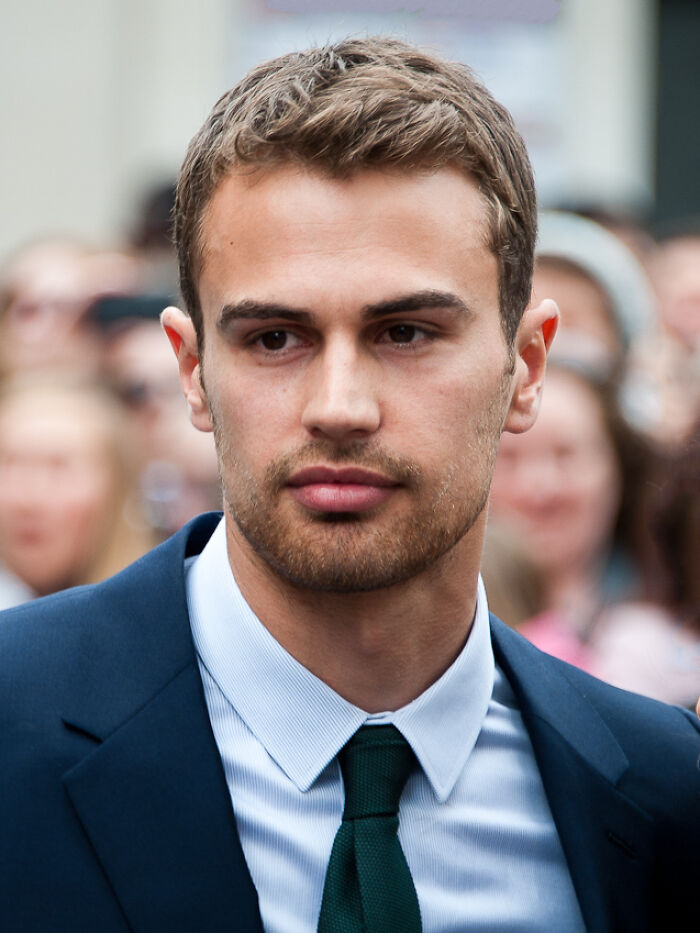 Theo James in a navy suit and green tie attending a public event, showcasing his bio and career highlights.