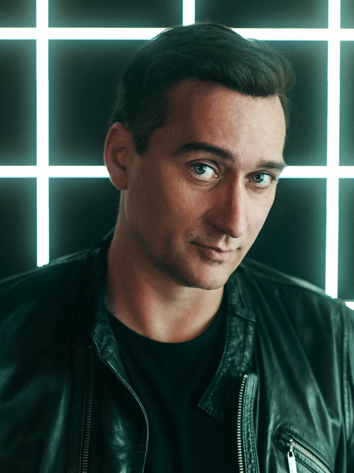 Paul van Dyk in a black leather jacket, posing confidently against a glowing grid background.