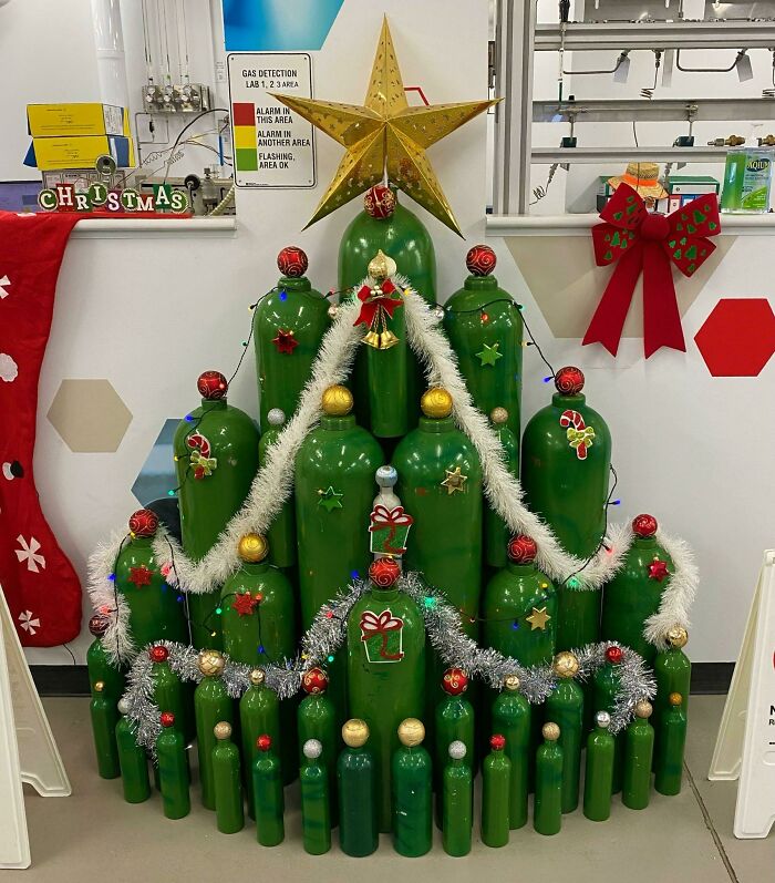 Creative workplace Christmas decorations featuring green bottles arranged as a tree with ornaments, garlands, and a star on top.