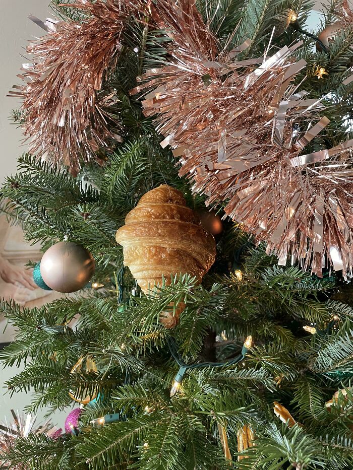 Christmas tree decorated creatively in a workplace with tinsel, lights, and a unique croissant ornament for festive inspiration.