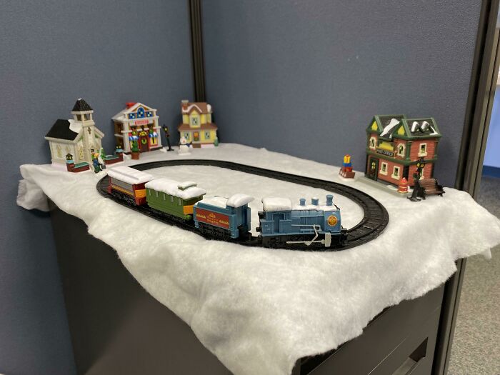 Miniature Christmas train set with snowy decorations and festive buildings in a creative workplace holiday display.