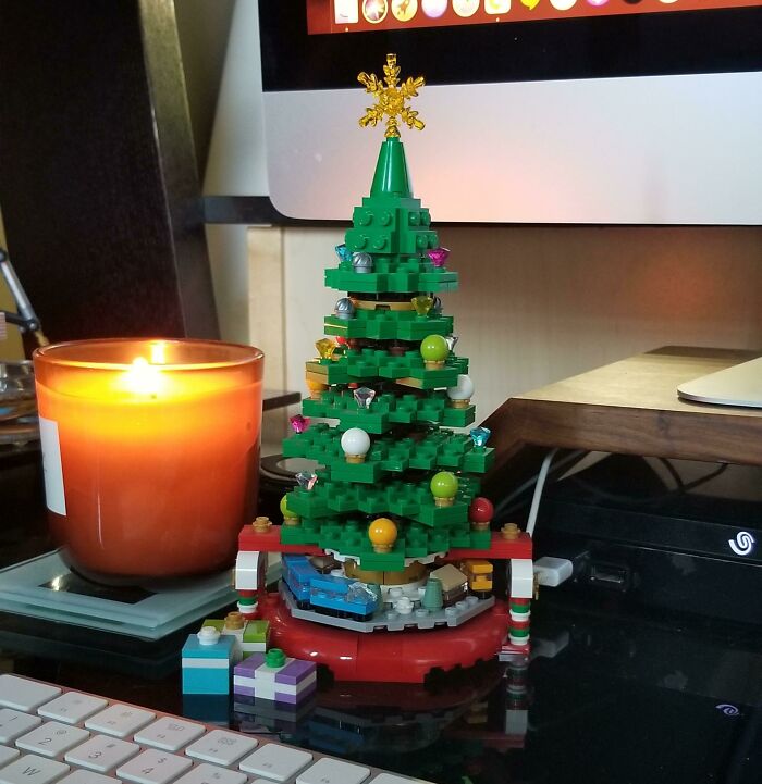 Creative workplace Christmas decorations featuring a LEGO Christmas tree with colorful ornaments and a lit candle on a desk.