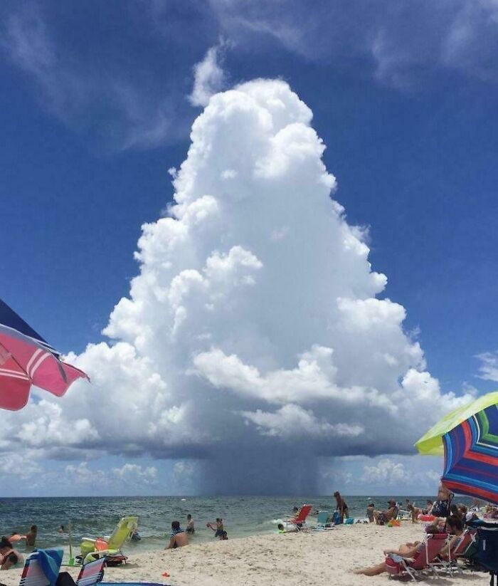 Massive towering cloud formation over beachgoers creating a striking image for megalophobia fear.