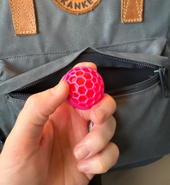 Hand holding a small pink toy ball in front of a gray backpack, perfect for last-minute gifts for unexpected guests.