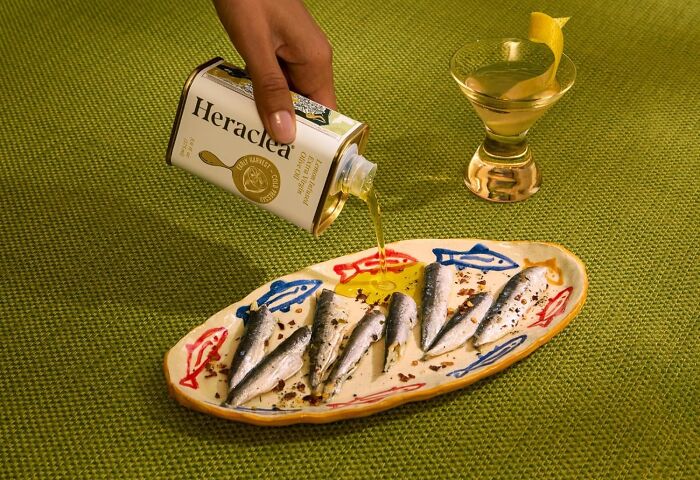 Hand pouring olive oil on sardines arranged on a decorative plate, a unique gift idea for the person who has everything.
