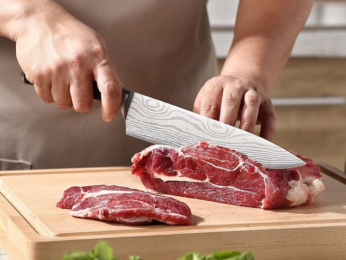 Person slicing raw meat with a chef knife on a wooden board, a unique gift for the person who has everything.