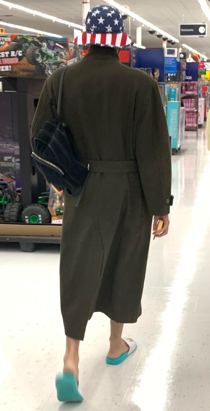Person wearing a long coat and American flag bucket hat in a Walmart aisle with toy trucks on display.