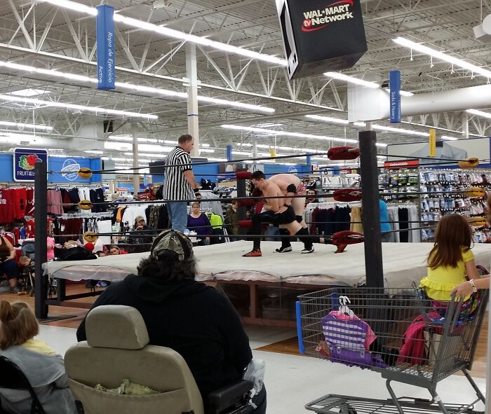 Wrestling match taking place inside a Walmart store with shoppers watching near clothing and household aisles.