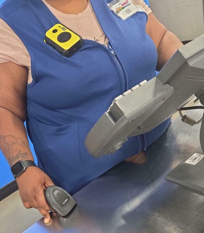 Walmart employee in blue vest using a barcode scanner at checkout counter inside the store.