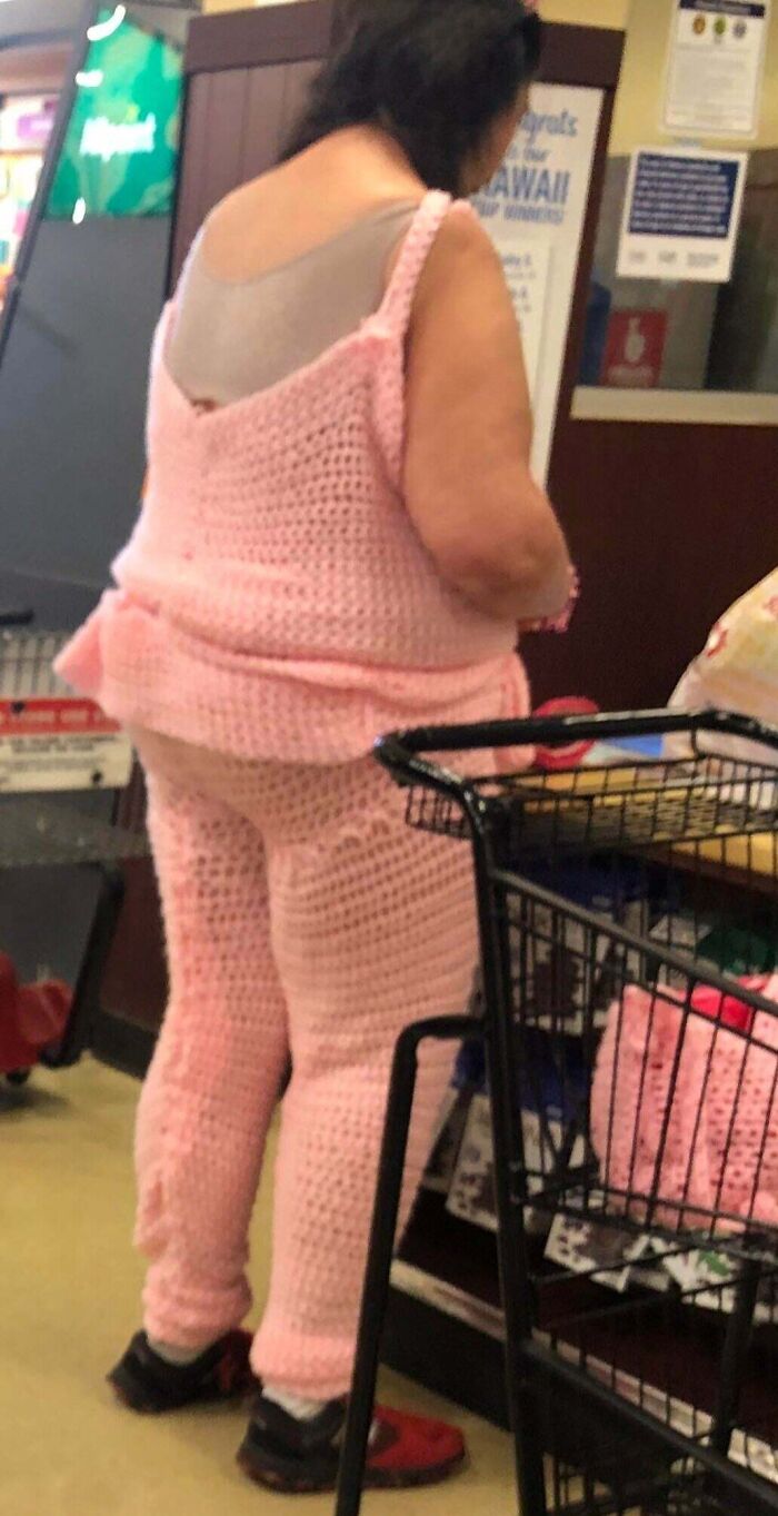 Woman in pink crocheted outfit shopping at Walmart with a cart filled with matching crocheted items.
