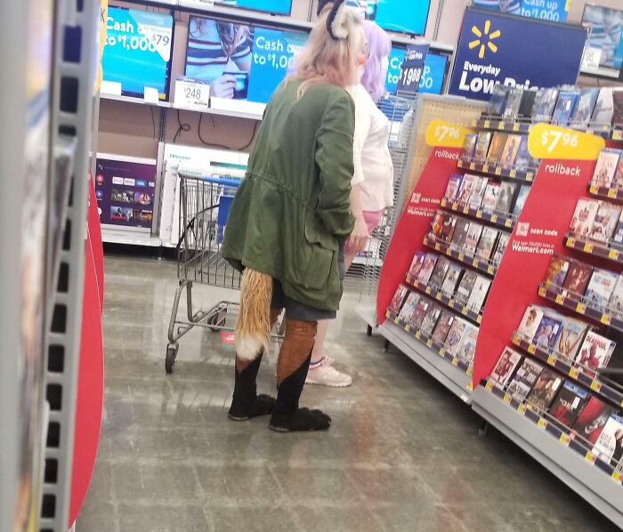 Customer wearing animal costume accessories browsing DVDs inside Walmart store aisle with everyday low prices signs.