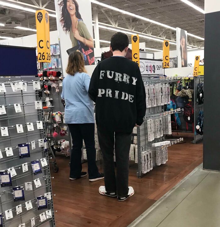 Shoppers inside a Walmart aisle with one person wearing a black shirt that says furry pride.