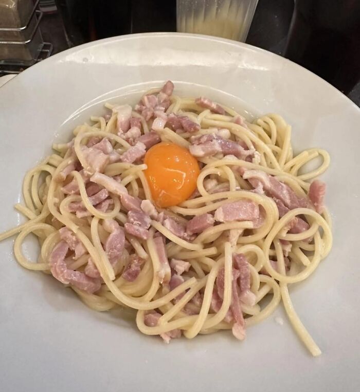 Plate of spaghetti carbonara with raw egg yolk and ham pieces, an example of food pics that deserve to be shamed online