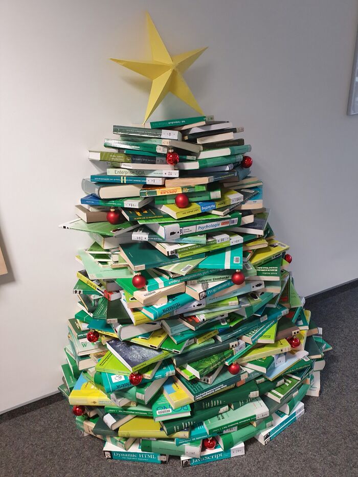 Creative workplace Christmas decorations featuring a unique tree made of stacked books with a star and red baubles.