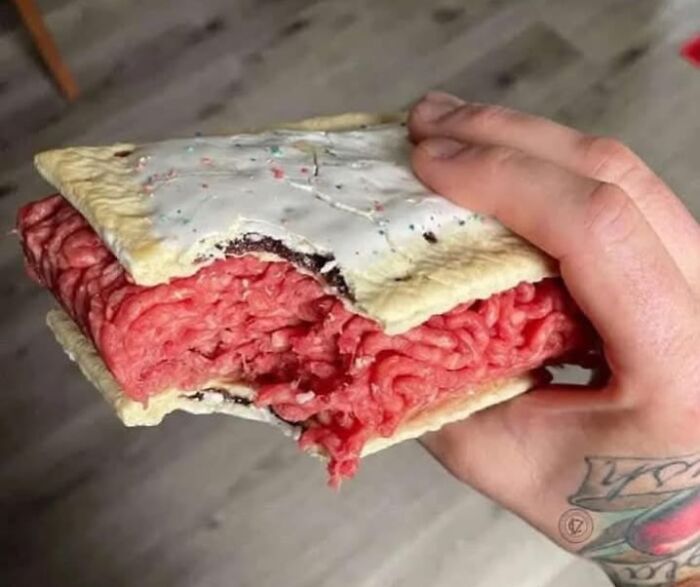 Uncooked ground meat inside a frosted pastry held by a tattooed hand, showcasing a food pic that deserves to be shamed online.