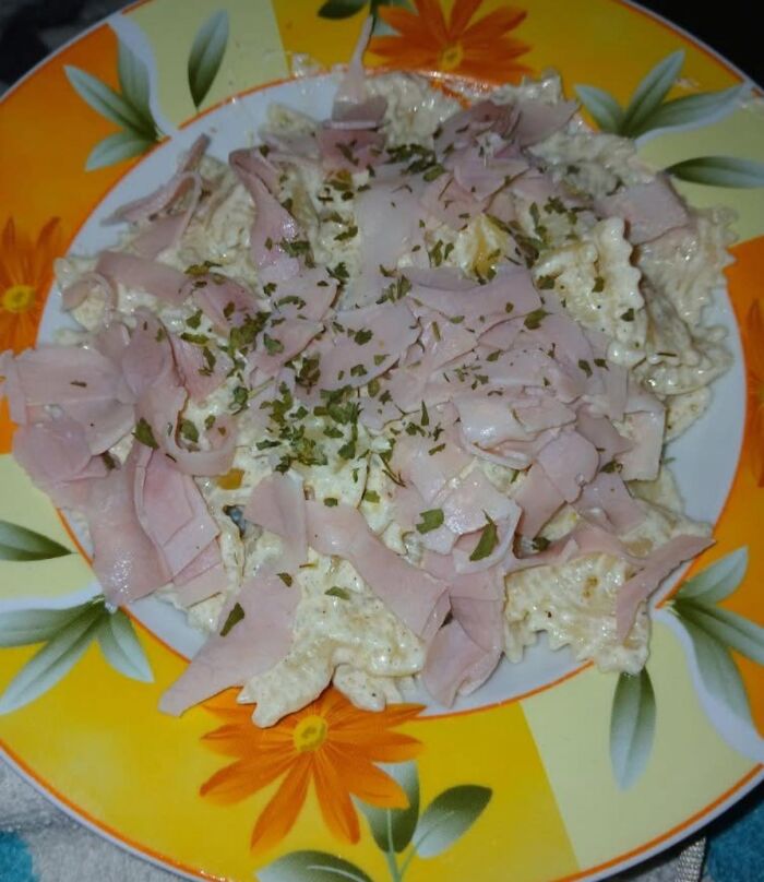Plate of farfalle pasta with ham and cream sauce topped with herbs, one of the food pics that deserve to be shamed online.