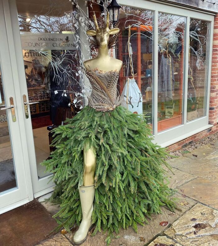 Creative Christmas decorations outside a store featuring a mannequin dressed in pine branch skirt and gold reindeer head.