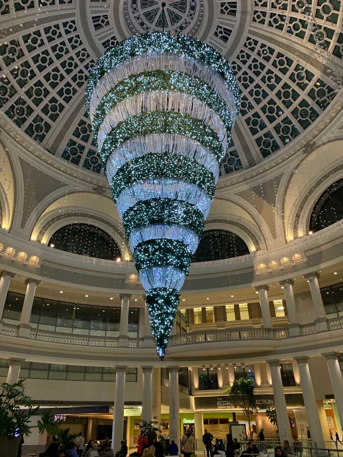 Inverted Christmas tree installation with bright lights and greenery displayed in a grand workplace lobby decoration.