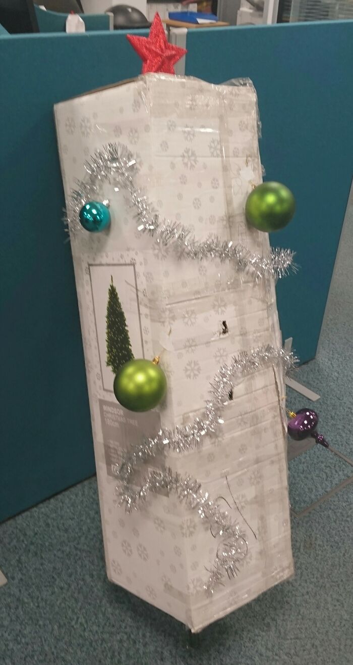 Creative workplace Christmas decorations with ornaments and tinsel on a boxed artificial tree in an office cubicle.