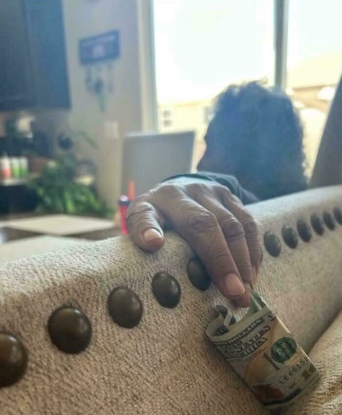 Hand holding a rolled dollar bill tucked under couch buttons in a funny picture capturing weirdness in 2025.