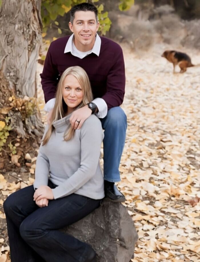 Couple posing outdoors on autumn leaves with dog in background, capturing a hilariously awkward family Christmas photo moment.